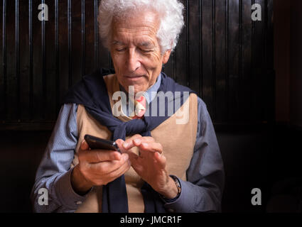 Felice vecchio uomo guarda al suo telefono cellulare le foto dei nipoti. Sorridente. Foto Stock