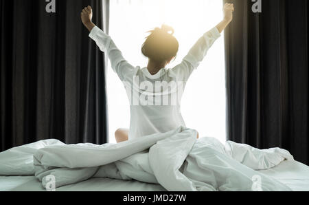 Donne asiatiche riattivazione dallo stato di stop. Sono stretch se stessa al mattino sul weekend sedersi sul letto in camera di lusso in relax e concetto di fine settimana Foto Stock