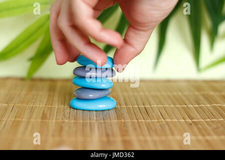 Una mano che ciottoli in stile Zen su un marrone pavimenti in bambù Foto Stock