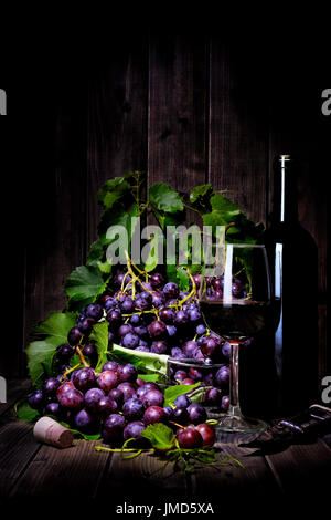 Rosso fresco grappolo di uva giacente su foglie su un vecchio tavolo di legno. Fotografato con luce tecnica di pittura Foto Stock