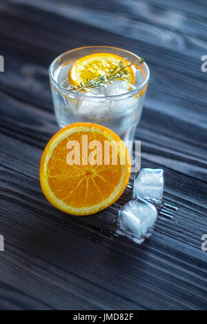 Un drink rinfrescante con Orange, cubetti di ghiaccio e rosmarino in un vetro su una tavola di legno scuro. Ancora la vita in un ristorante o un bar Foto Stock