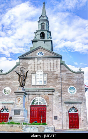 Ile D'Orleans, Canada - 1 Giugno 2017: Saint-Jean dipinte di rosso chiesa con architettura di pietra e Gesù Cristo statua, cielo blu in estate Foto Stock