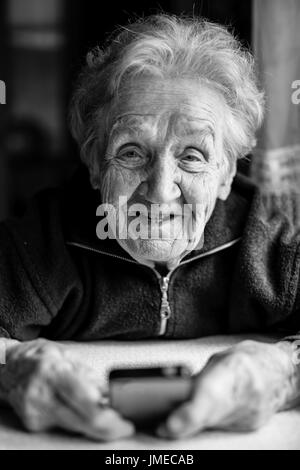 Ritratto di close-up di una donna anziana è la digitazione su telefono seduta sul tavolo. In bianco e nero della fotografia. Foto Stock