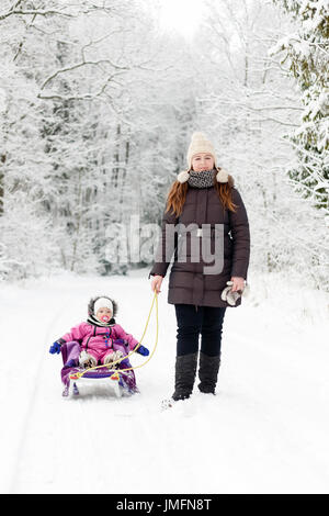 La madre è figlia di traino sulla slitta in inverno forest attraverso la neve Foto Stock