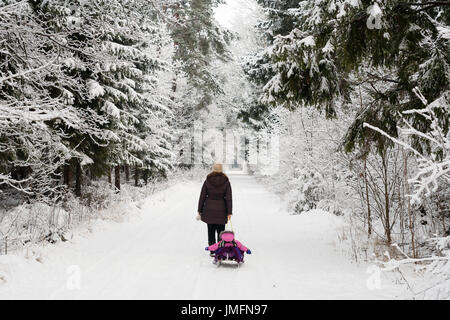 La madre è figlia di traino sulla slitta in inverno forest attraverso la neve Foto Stock