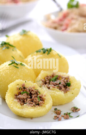 Gli gnocchi di patate ripiene di carne macinata servita su un piatto bianco, crauti con pancetta in background Foto Stock