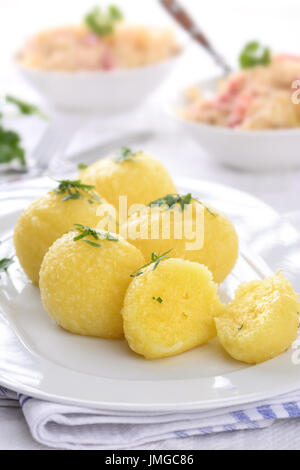 Cucinata fresca gnocchetti di patate servita su un piatto bianco, crauti con strisce di pancetta in background Foto Stock