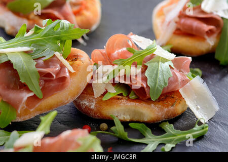 Pizza snack con prosciutto di Parma, foglie di rucola e parmigiano servito su un ardesia Foto Stock