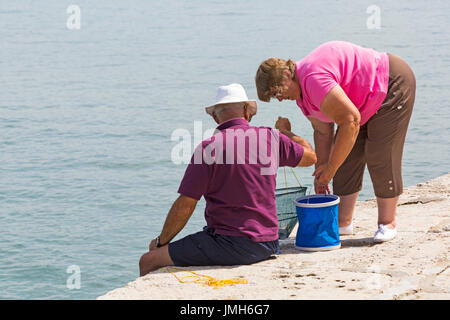 Uomo seduto sulla parete con cestello net pescato granchi la pesca con la donna a Lyme Regis, Dorset in luglio Foto Stock