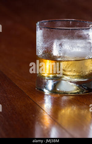 Blended scotch whisky servita in un corto di vetro con un grande cubo di ghiaccio è servita in un bar in legno top Foto Stock