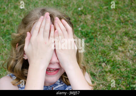 Bambina nascondere faccia dietro le mani Foto Stock