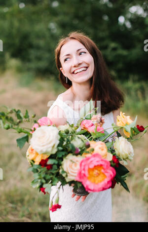 Bouquet, persone e composizioni floreali concetto - una giovane donna sorridente con capelli castani e bouquet colorati in mani, rosa peonie, rose, garofani, Foto Stock