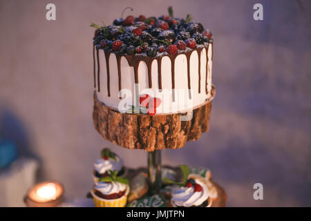 Torta e i tortini con frutti di bosco su un ripiano di legno al lume di candela. Foto Stock