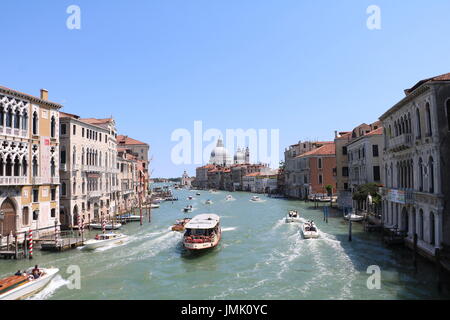 Barche accelerando attraverso un canale su un luminoso giorno chiaro, tra gli edifici storici di Venezia, Italia Foto Stock