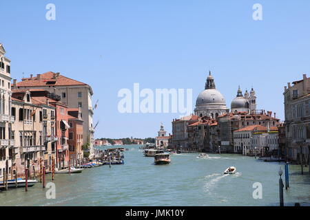 Barche accelerando attraverso un canale su un luminoso giorno chiaro, tra gli edifici storici di Venezia, Italia Foto Stock