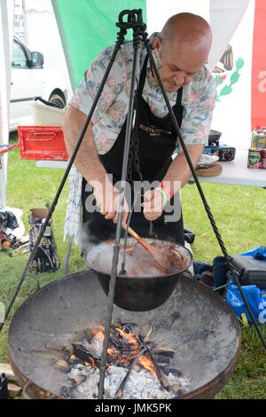 Un uomo di carbone da coke chili con carne oltre ad aprire il fuoco in una ghisa pentola Gower chili Festival Glamorgan Foto Stock