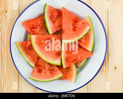 Piastra di tagliare segmenti di cocomero contro un pino di luce sullo sfondo di legno Foto Stock