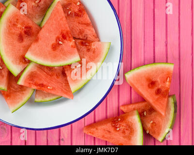 Piastra di tagliare segmenti di cocomero contro una rosa di sfondo di legno Foto Stock