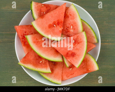 Piastra di tagliare segmenti di cocomero contro un verde sullo sfondo di legno Foto Stock