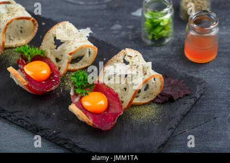 Carni bovine indurita su crostini di pane con tuorlo d'uovo e formaggio parmedgano Foto Stock