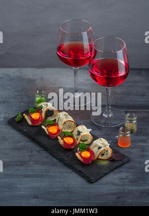 Antipasti - salumi, pane croccante, tuorlo d'uovo e formaggio - sulla scheda di pietra con due bicchieri di vino Foto Stock