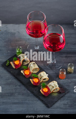 Antipasti - salumi, pane croccante, tuorlo d'uovo e formaggio - sulla scheda di pietra con due bicchieri di vino Foto Stock