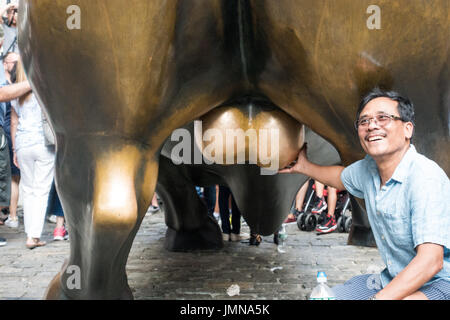 I vecchi turisti asiatici in ginocchio e toccando la carica Bull di testicoli in posa per una fotocamera al Quartiere Finanziario di Manhattan, NY Foto Stock