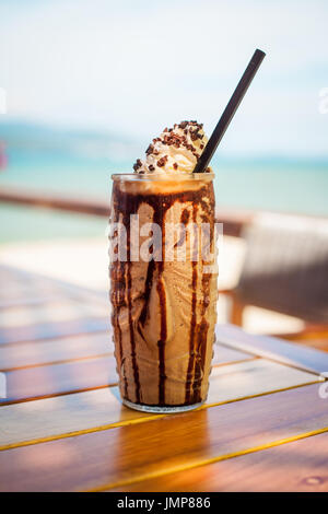 Iced mescolate il latte e la cioccolata frappucino con panna montata sulla spiaggia Foto Stock