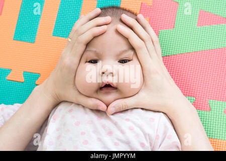 Le mani di Madre schiacciamento sulla faccia del suo piccolo grazioso baby in schiuma eva in camera da letto Foto Stock