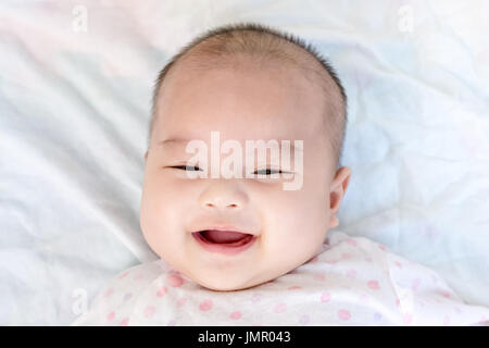 Ritratto di un piccolo bambino adorabile bambina giacente sul retro sulla coperta e cercando nella fotocamera in ambienti interni Foto Stock