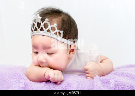 Ritratto di un piccolo bambino adorabile bambina con la corona che giace sulla pancia sulla coperta Foto Stock