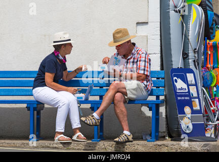 Coppia seduta sul banco di mangiare pesce e patatine a Lyme Regis, Dorset in luglio Foto Stock