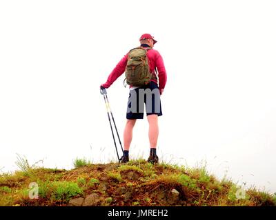 L uomo nella nube di nebbia. Escursionista in rosa nero sportswear e poli stand sul picco di montagna roccia. Intorno al forte nebbia. In condizioni di scarsa visibilità Foto Stock