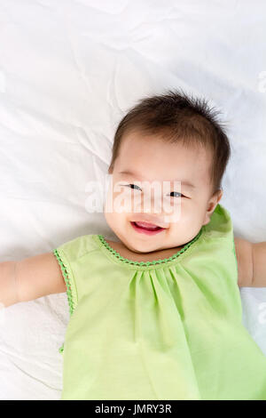 Ritratto di un piccolo bambino adorabile bambina giacente sul retro sul letto e cercando nella fotocamera in ambienti interni Foto Stock