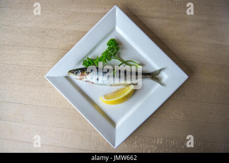 Una sardina, 1 ciuffo di prezzemolo e un cuneo di limone su una piastra. Foto Stock