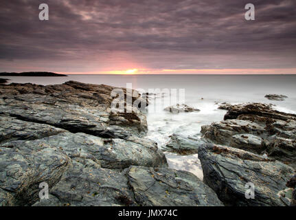 Le aspre rocce lungo la costa nord di Anglesey, Galles, vicino Cemlyn, sono la base per questo tramonto shot, che guarda al mare. Foto Stock