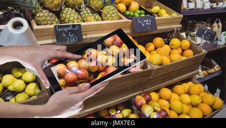 Composito Digitale delle mani di fotografare le mele attraverso la tavoletta digitale al negozio di alimentari Foto Stock