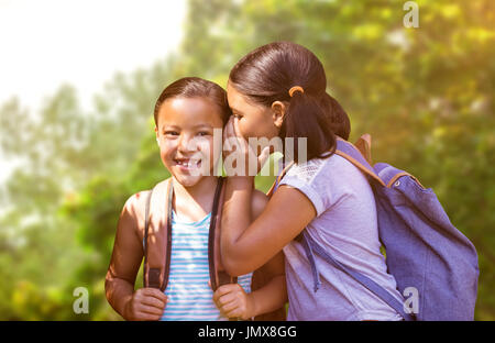 Ragazza con zaino whispering in orecchio amico contro gli alberi della foresta Foto Stock