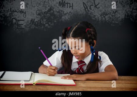 Testo sulla lavagna nera contro la scolaretta facendo il suo dovere contro la lavagna Foto Stock