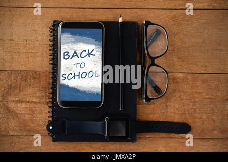 Digital immagine composita di ritorno a scuola su testo blu vernice spray contro gli accessori personali sul tavolo di legno Foto Stock