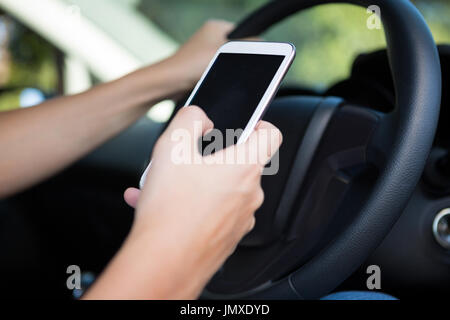 Le mani della donna che utilizza il telefono cellulare mentre si è alla guida di un veicolo Foto Stock