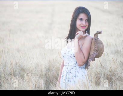 Bella donna con cappello estivo nel campo di grano al tramonto Foto Stock