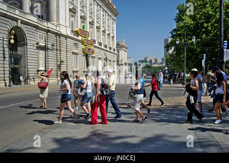 Gruppo turistico di attraversare una strada vicino a al Palazzo Reale di Madrid. Tour guida porta il gruppo tenendo un ombrello rosso. Foto Stock