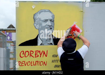 Bristol, Regno Unito. 29 Luglio, 2017. Un artista grafitti vestito come un poliziotto lavora su una foto di Jeremy Corbyn. Parte del Bristol Upfest 2017, il più grande d'Europa, gratuito, street art & graffiti festival, che attrae oltre 300 artisti pittura 35 luoghi in tutta Bristol da 29th-31st Luglio 2017 Credit: stephen Hyde/Alamy Live News Foto Stock