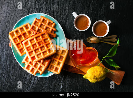 La prima colazione con cialde belghe, confettura di albicocca e caffè su una pietra nera sullo sfondo Foto Stock