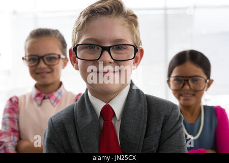 Ritratto di bambini come business executive sorridere mentre in piedi in ufficio Foto Stock