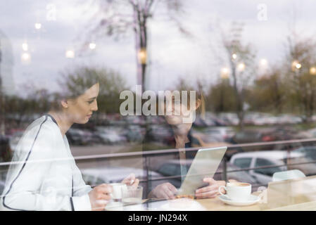 Donna sorridente amici discussioni su tavoletta digitale mentre è seduto in cafe visto attraverso la finestra Foto Stock