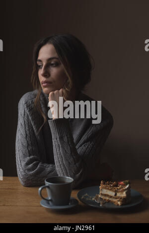 Contemplato il giovane donna con la mano sul mento seduta a tavola Foto Stock