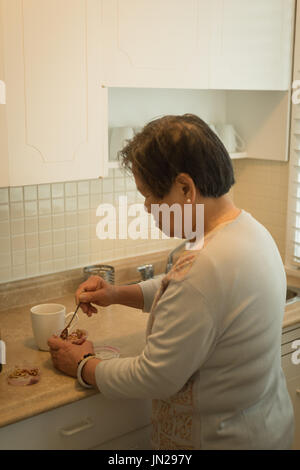 Vista laterale della donna senior di preparazione di caffè permanente, mentre in cucina a casa Foto Stock