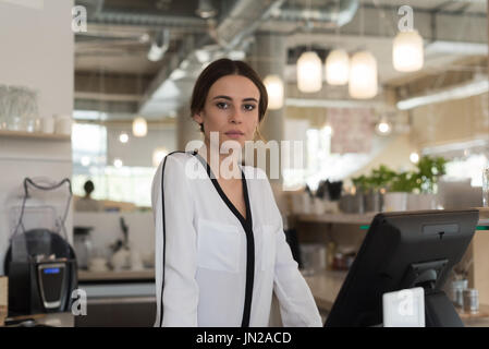 Ritratto di giovane donna proprietario in piedi alla cassa Foto Stock